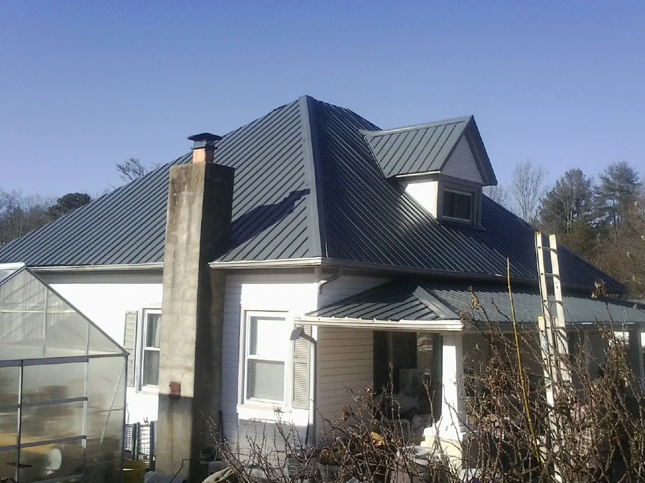 Dark blue standing seam metal roof on a white farmhouse with dormer — Slate & Tile Roof Repair by Roofing Brothers in Paynesville