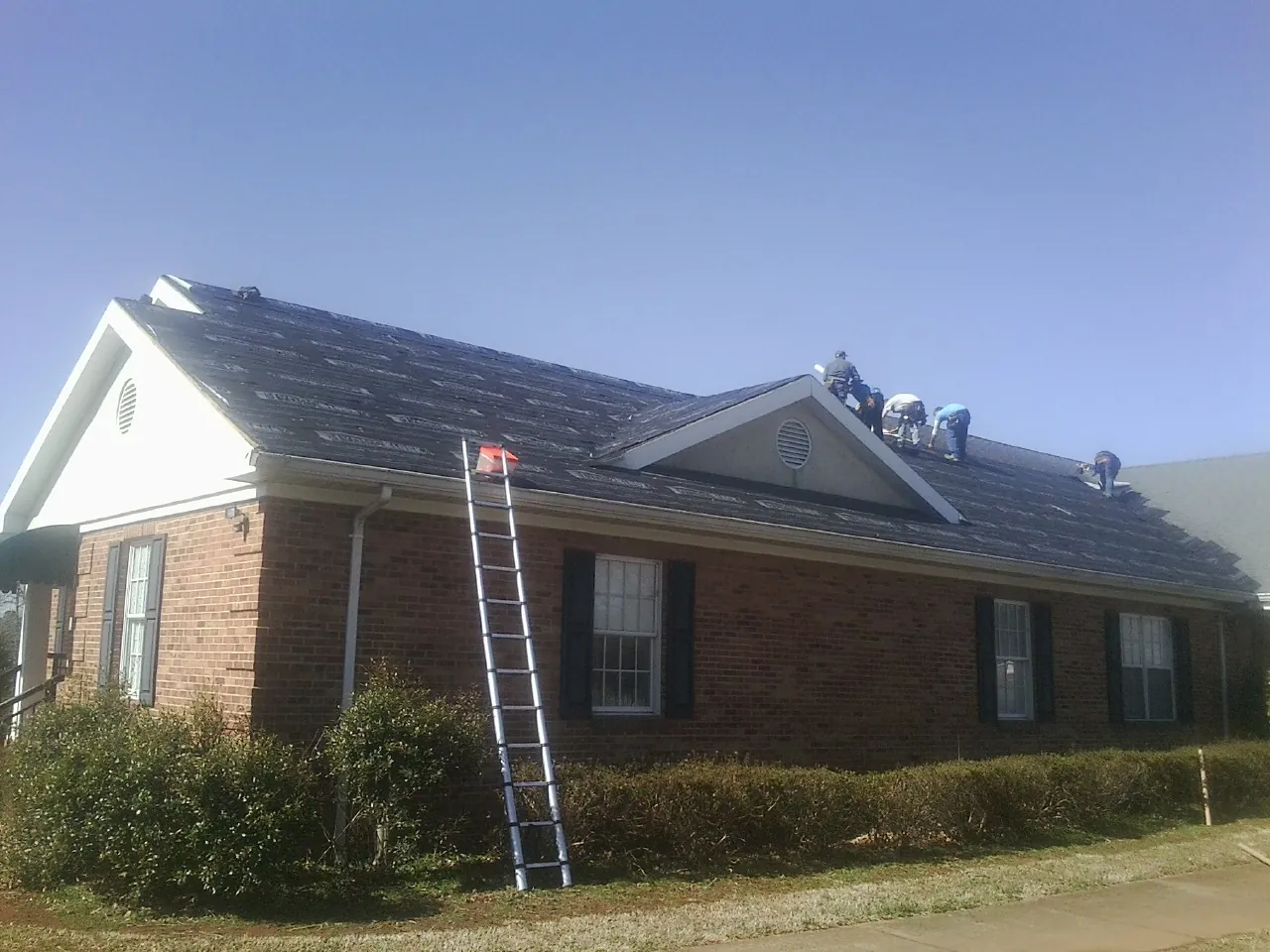 Crew tearing shingles off a brick ranch roof with a ladder set — Metal Roof Repair work by our crew in Paynesville