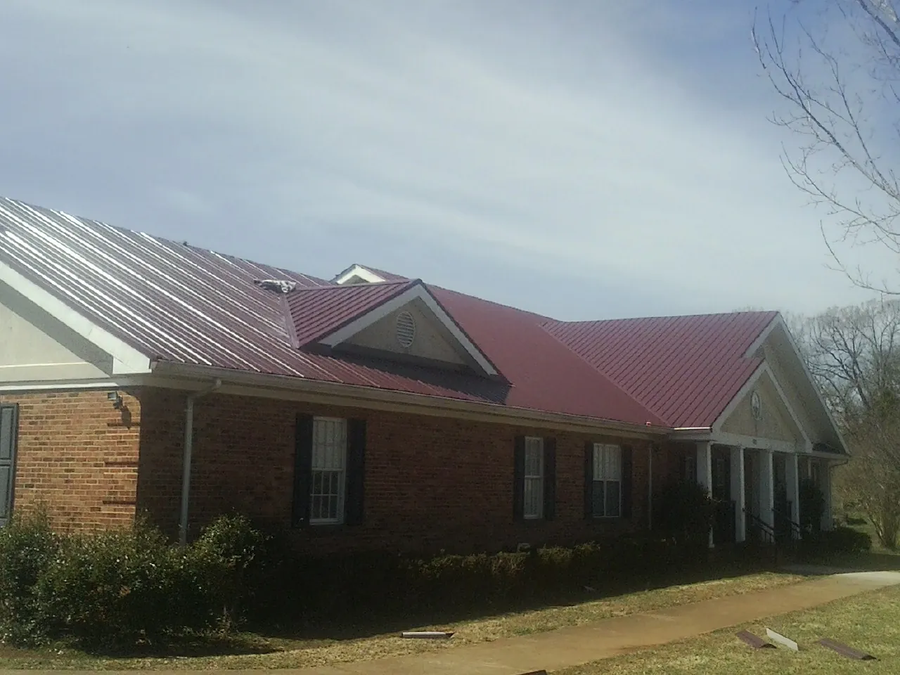 Red metal roof with gabled entries on a long brick building, from a Hail Damage Roof Repair job in Paynesville