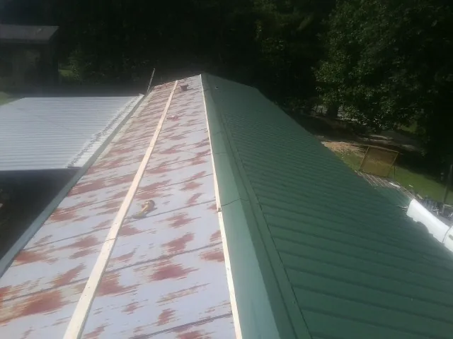 Old rusted panels beside newly installed green metal roofing in Paynesville