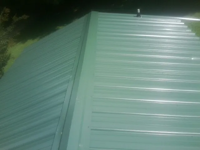 New green metal panels meeting at the ridge of a roof — Flat Roof Repair work by our crew in Paynesville