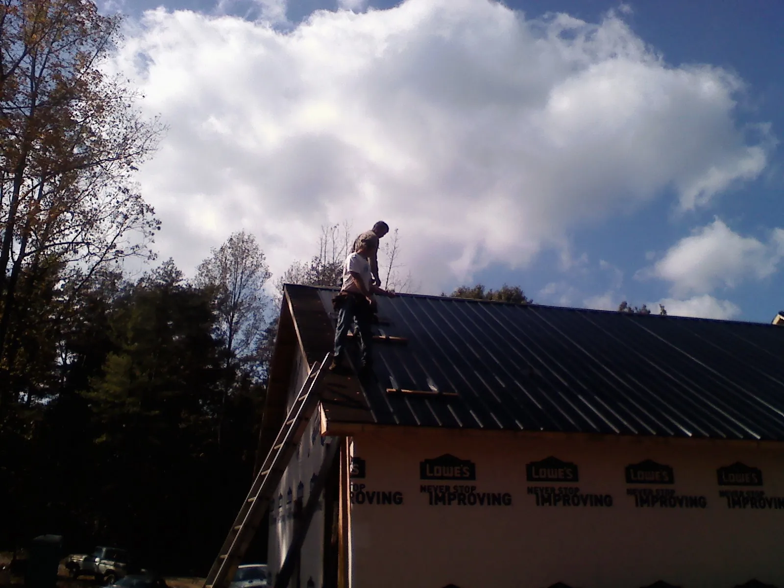 Roofer fastening dark metal panels high against a cloudy sky, from a Roof Inspection job in Paynesville