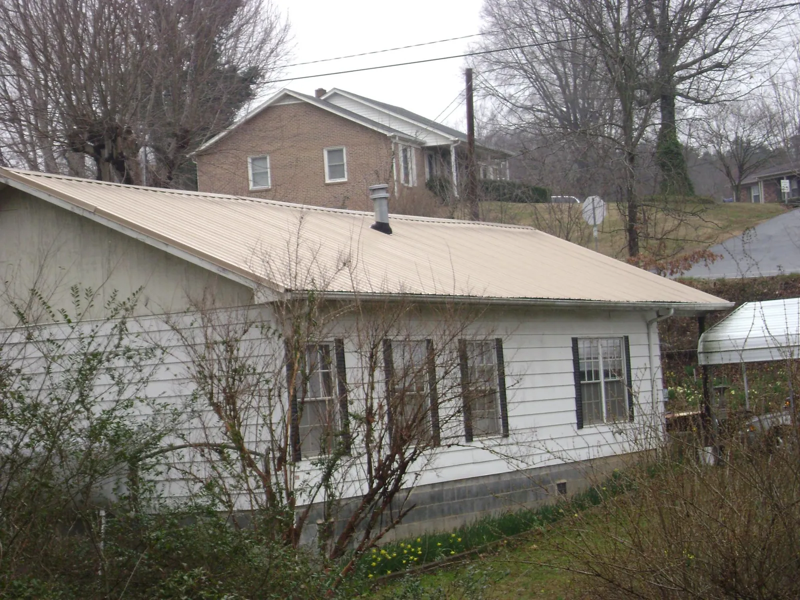 Tan metal roof on a white sided house set into a hillside — Commercial Roofing by Roofing Brothers in Paynesville