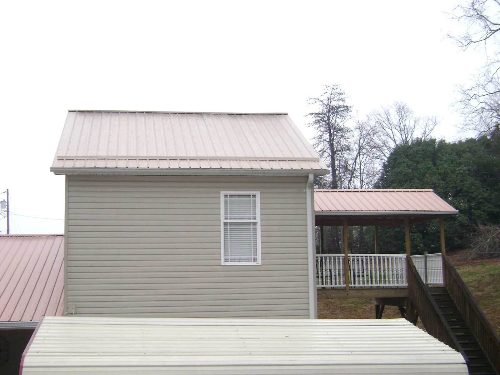 Tan metal roofs on a two story addition and attached porch, from a Roof Replacement job in Paynesville